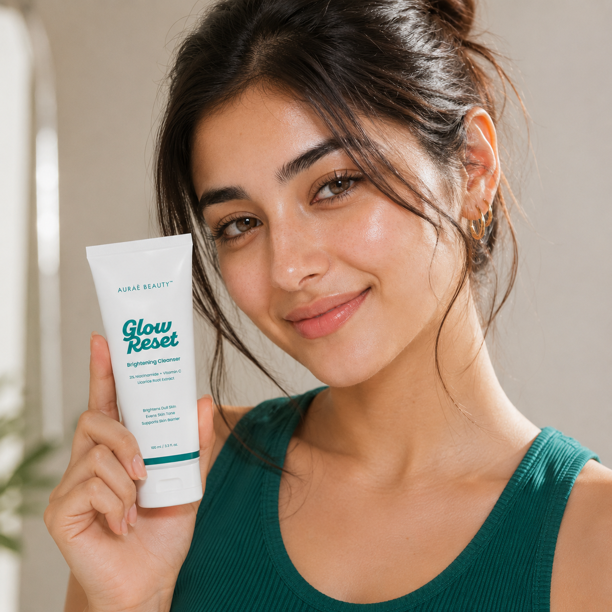 A woman holding a Glow Reset Brightening Cleanser by Auraé Beauty against a soft beige background.
