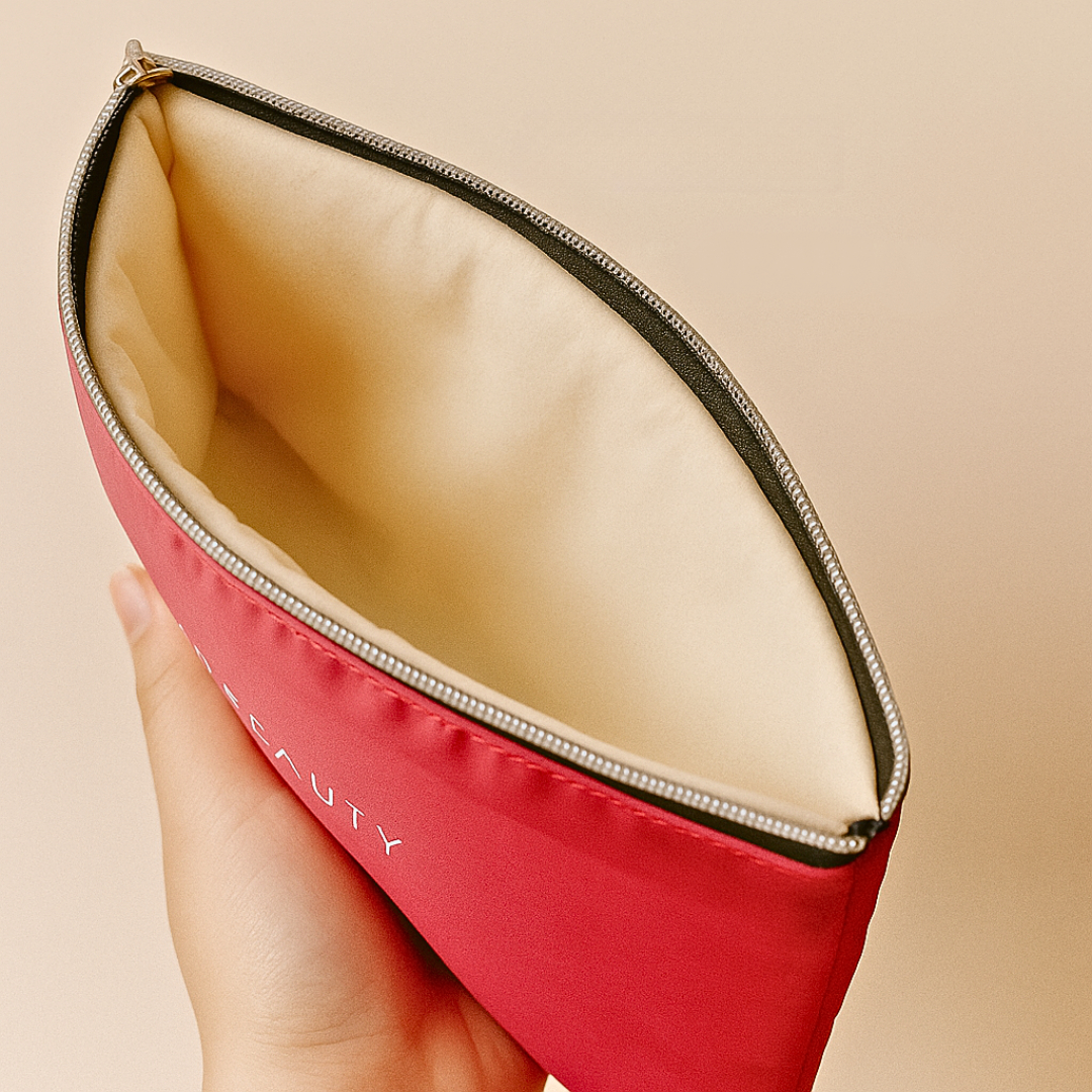 Red makeup pouch with beige interior held by a hand against a beige background