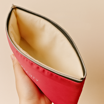 Red makeup pouch with beige interior held by a hand against a beige background